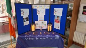 A display with blue boards features papers and photos about Irish Catholic education. Two lanterns and a candle sit on a table covered with a CEIST: Catholic Education—An Irish Schools Trust cloth. An Irish flag is on the left.